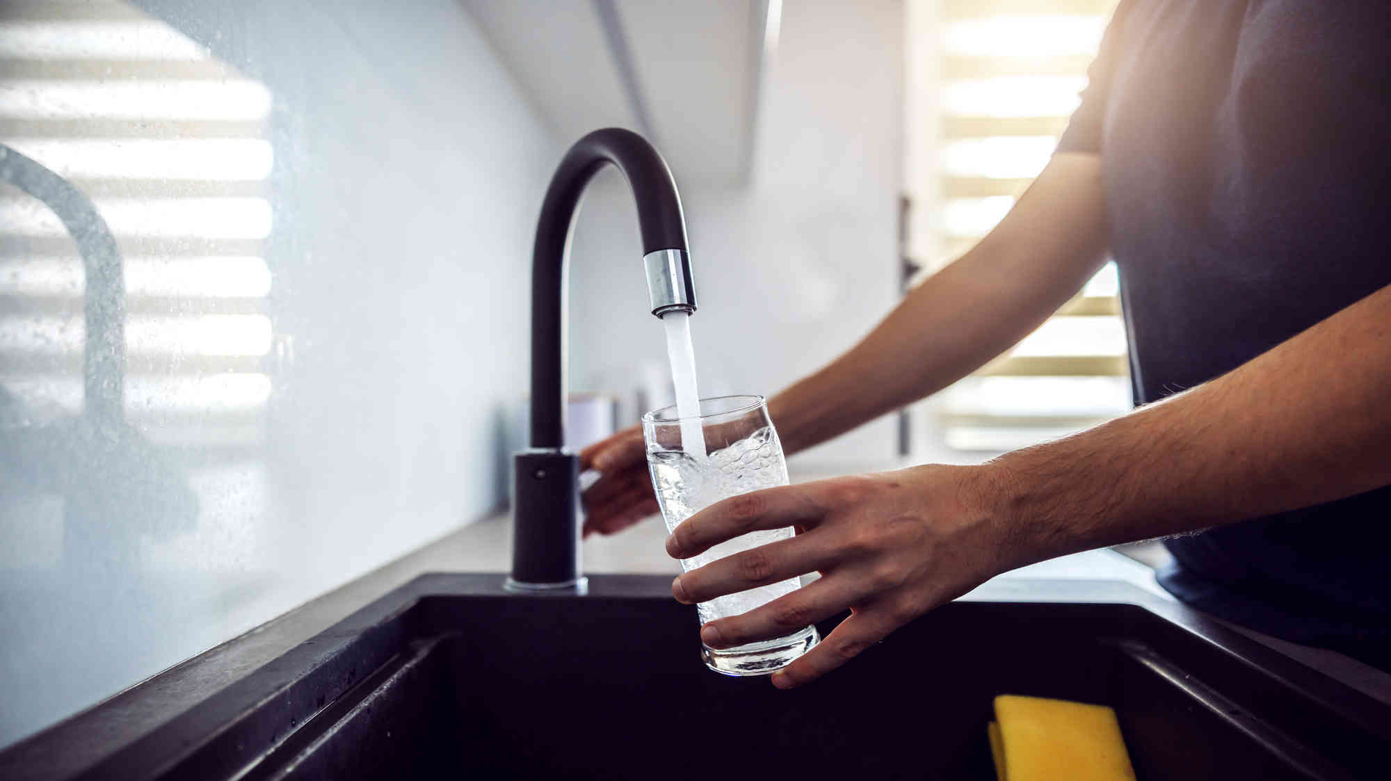 Person by a sink pouring water into a glass from a faucet